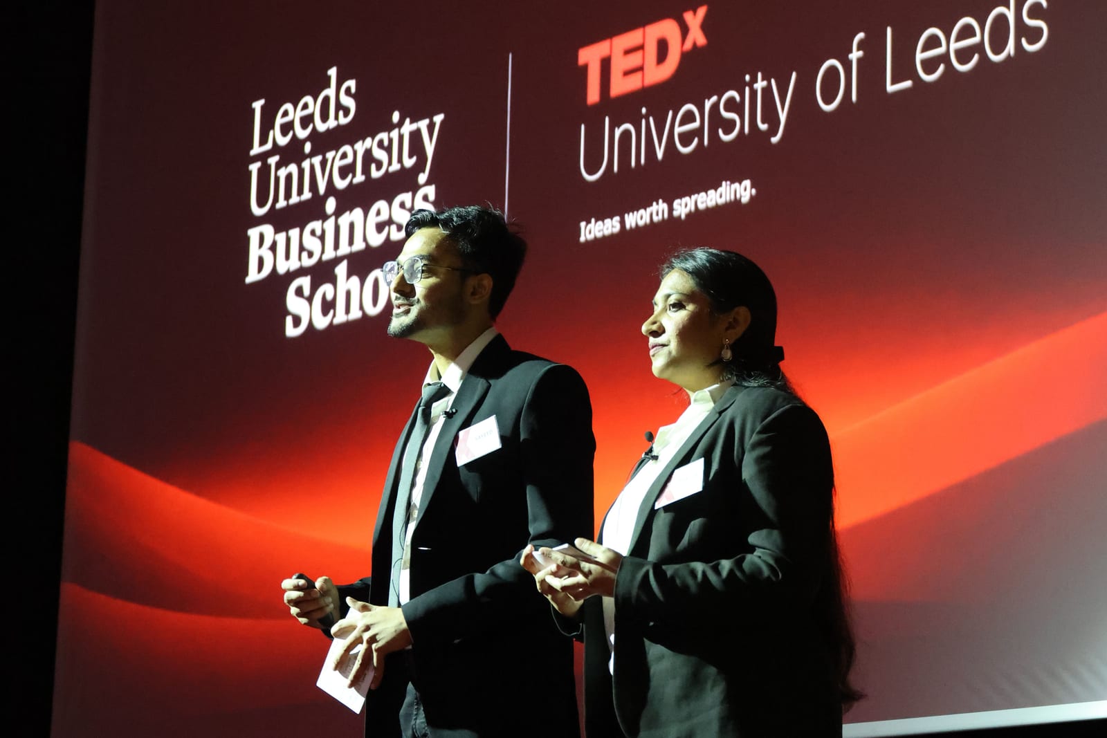 Event hosts on stage in front of the TEDx University of Leeds and Leeds University Business School screen