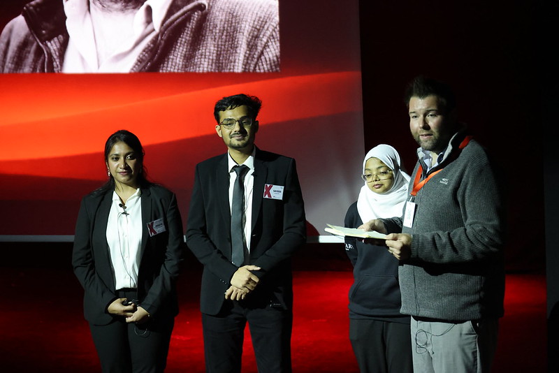 A presenter reading from a card on stage beside the event hosts