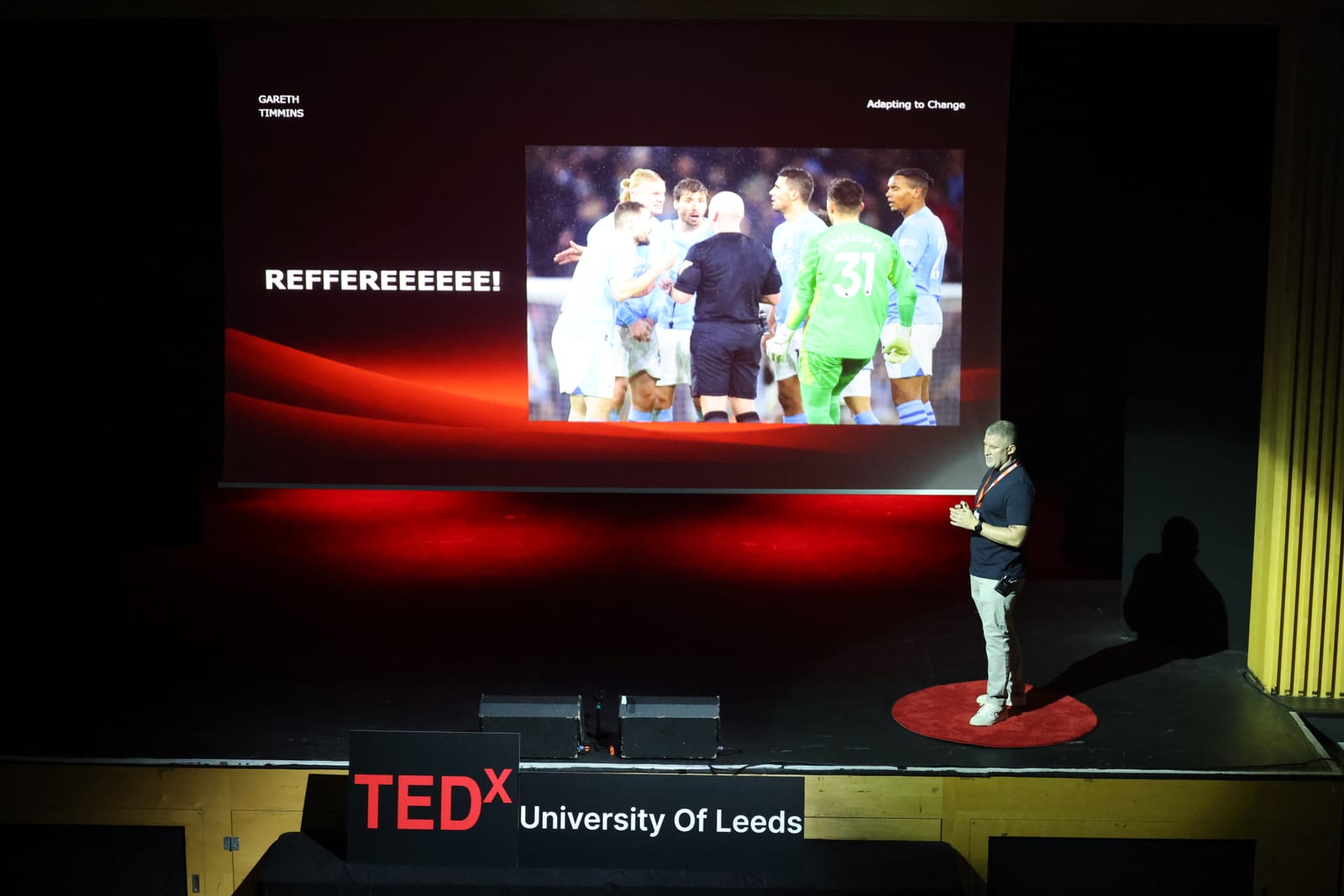Gareth Timmins speaking on stage in front of his slide on adapting to change