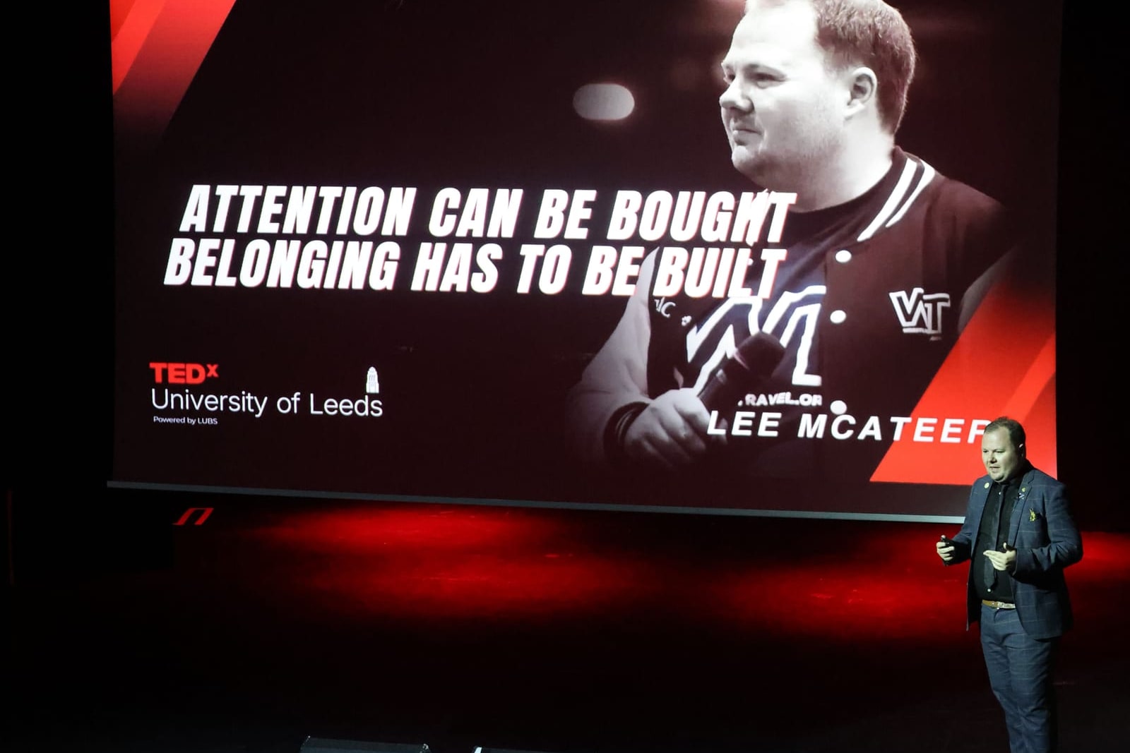 Lee McAteer speaking on stage in front of his slide: Attention can be bought, belonging has to be built