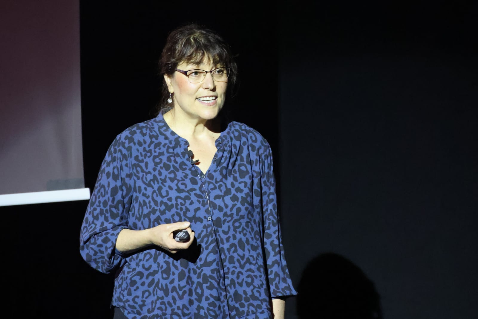 A speaker presenting on stage with a slide clicker in hand